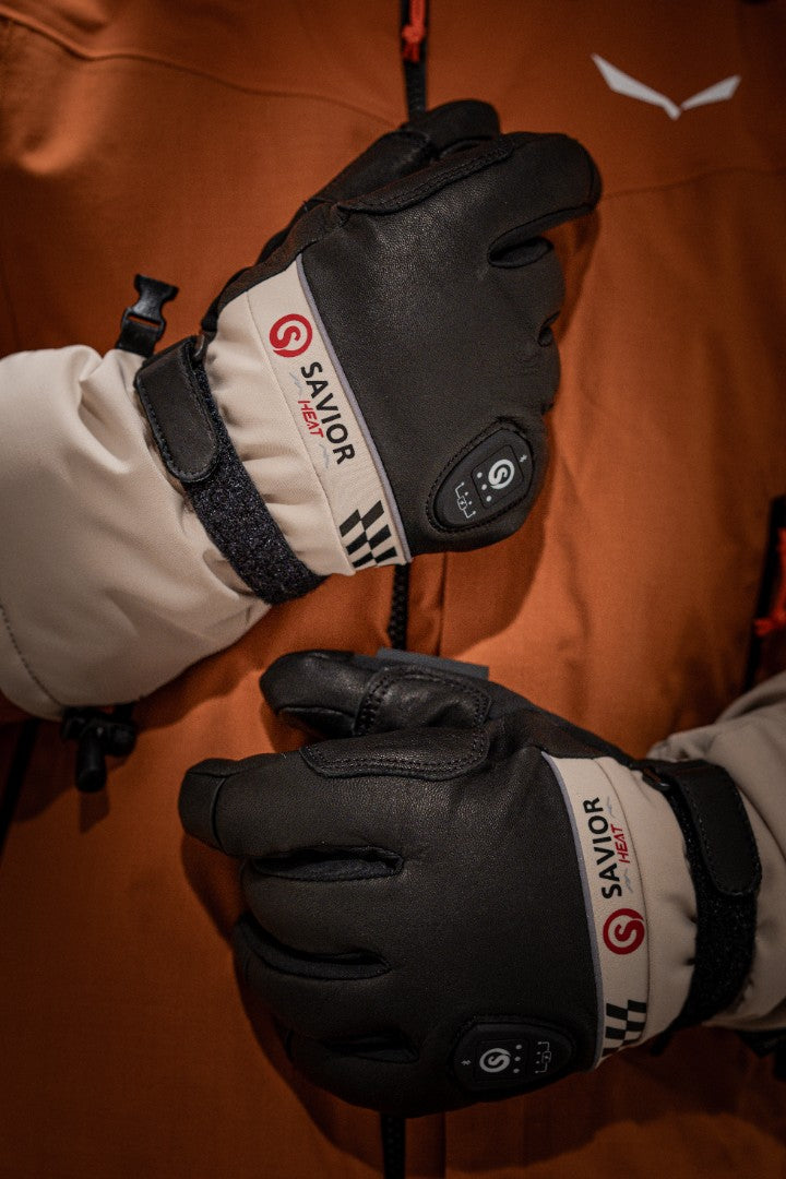 A pair of Savior heated gloves, designed for winter sports and cold weather, with temperature control buttons visible on the wrist. The gloves provide warmth and protection for skiers and outdoor enthusiasts in extreme cold conditions