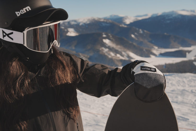 Person wearing Savior heated ski gloves holding a snowboard in snowy mountains
