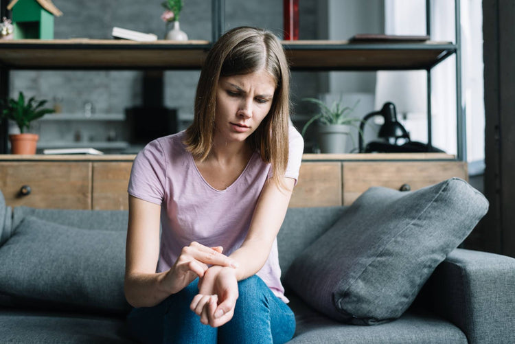 Woman experiencing symptoms of Raynaud's disease, such as cold hands and discomfort, while sitting on a couch