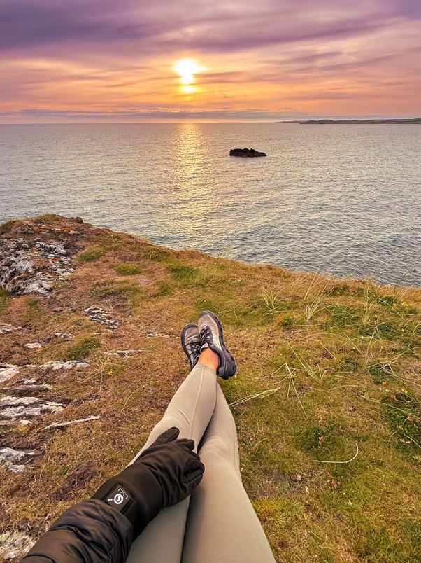 Person wearing heated gloves enjoying a sunset view by the coast during autumn.