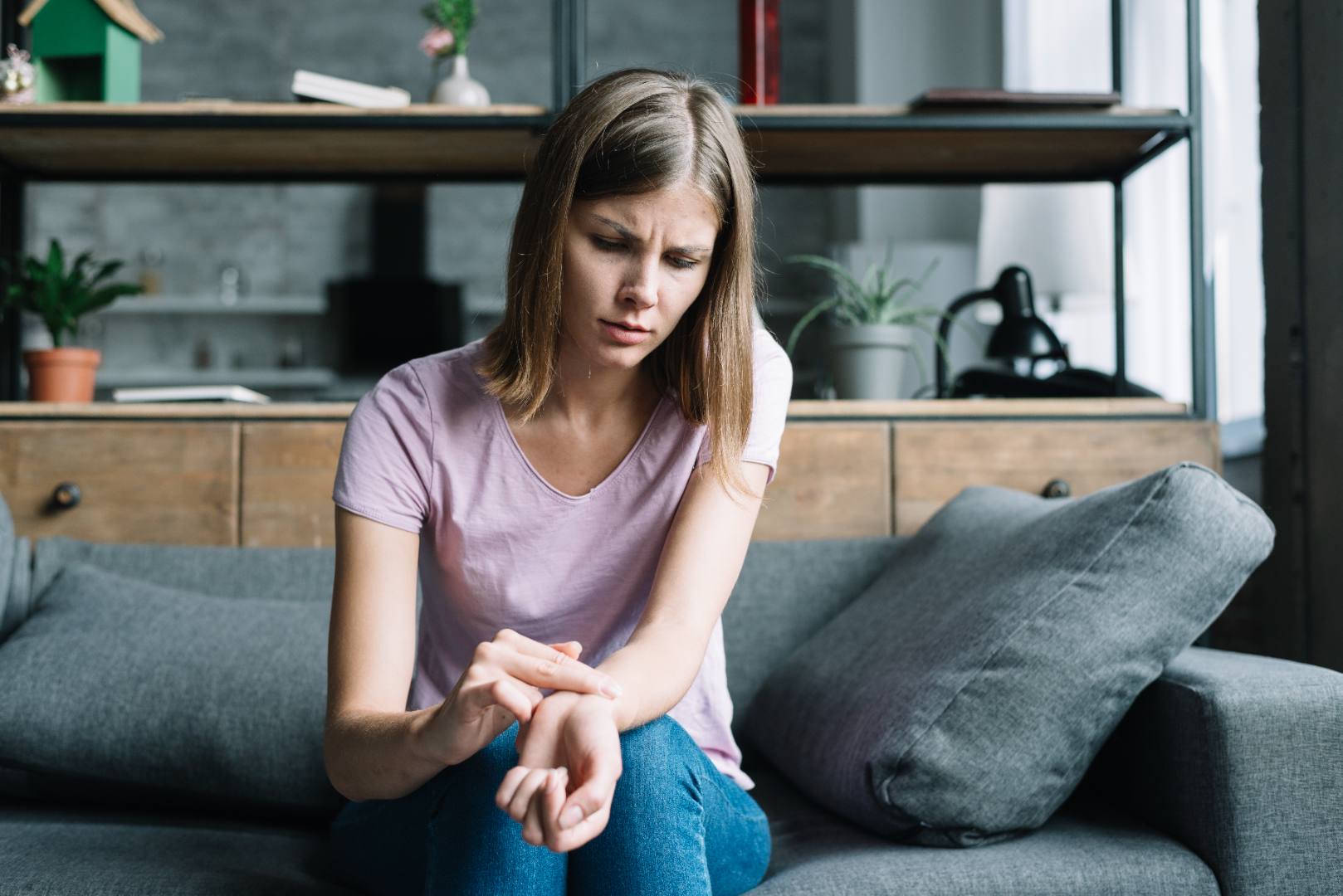 Woman experiencing symptoms of Raynaud's disease, such as cold hands and discomfort, while sitting on a couch