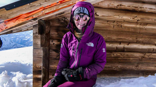 Woman wearing heated gloves in winter snow, sitting outside with The North Face jacket and ski goggles